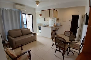 A living room with a sofa and chairs, a dining table with chairs, a kitchen with cabinets and appliances, and a sliding door.