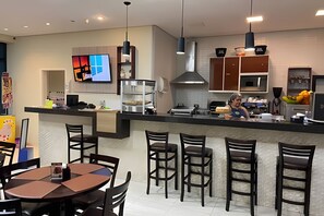 Una cocina moderna con barra, equipada con una televisión grande, varias estaciones de cocina y un área de estar con mesas y sillas.