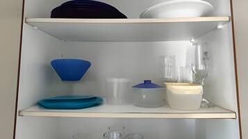 A kitchen cabinet with shelves holding various kitchenware, including bowls, a blender, and glasses.