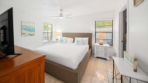 Ein Hotelzimmer mit Bett, Fernseher, Schreibtisch und einem Fenster mit Jalousien.