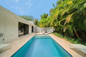A swimming pool with a patio area, surrounded by lush greenery and a white building. - 2219 Managed by Brampton Park (Delray Beach)