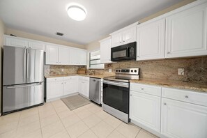 A kitchen with white cabinets, stainless steel appliances, a granite countertop, and a tiled floor. - 2219 Managed by Brampton Park (Delray Beach)