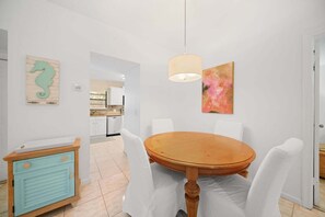 A dining area with a round wooden table, white chairs, a pendant light, and a painting on the wall. - 2219 Managed by Brampton Park (Delray Beach)