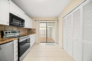 Una cocina compacta con armarios blancos, microondas, estufa y lavavajillas.