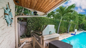 Eine Außenküche mit Grill, Liegestuhl am Pool und einer Holz-Pergola.