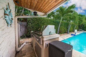 An outdoor kitchen with a grill, a poolside chair, and a wooden pergola. - 1650 Managed by Brampton Park (Pompano Beach)