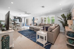 A modern living room with a sectional sofa, a flat-screen TV, and a dining area with a table and chairs. - 1650 Managed by Brampton Park (Pompano Beach)