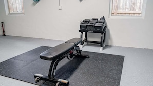 Ein Fitnessraum mit Langhantelbank, Kniebeugeständer und einem kleinen Fenster.