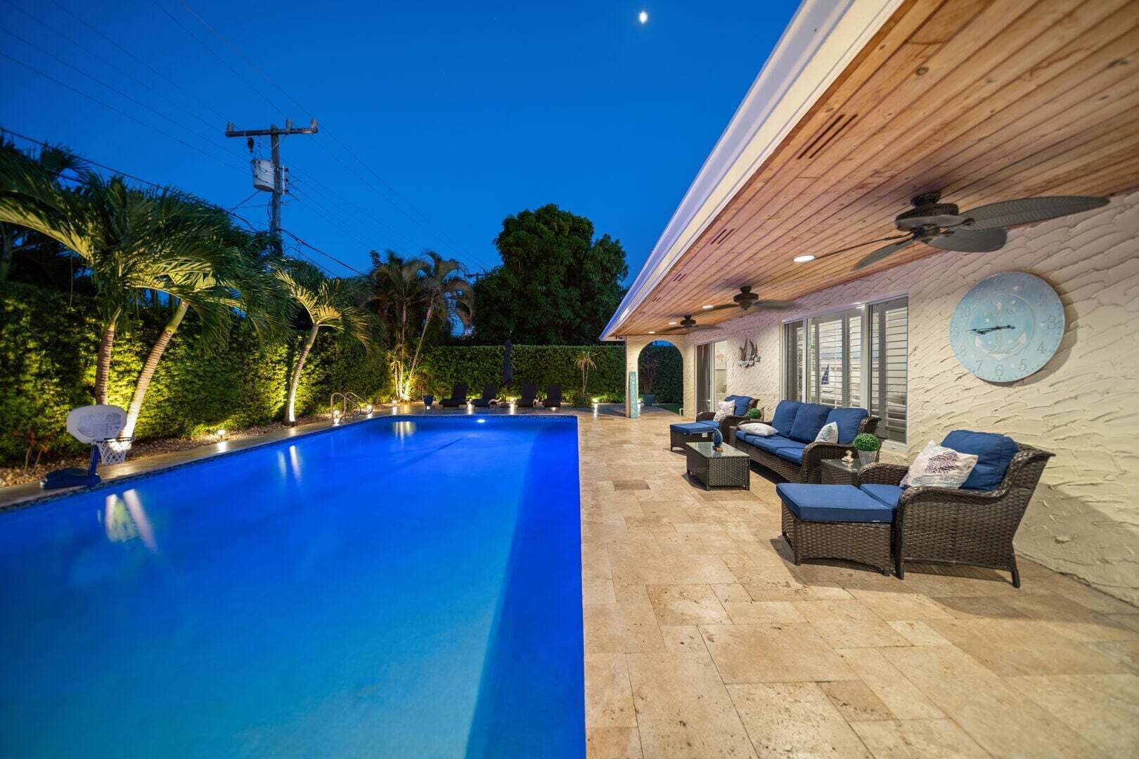 En swimmingpool med en terrasse, udendørs møbler og et ur på væggen.