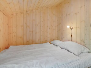 Une pièce aux murs en bois, un lit avec une literie blanche et un luminaire fixé au mur.