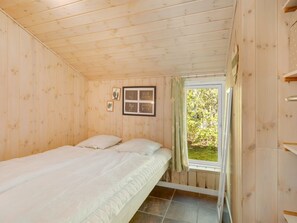 Een eenpersoonskamer met houten wanden, een raam met gordijnen en een lijst met een afbeelding aan de muur.