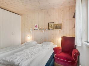 A bedroom with a bed, a red chair, wooden walls, and a shelf with pictures and candles.