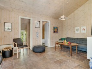 Een kamer met houten lambrisering, een bank, een tafel met drankjes, een stoel en een klein pouf.