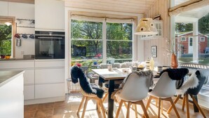 Une cuisine moderne avec des meubles blancs, un coin repas comprenant une table et des chaises, et de grandes fenêtres offrant une vue sur l’extérieur.