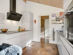 Une cuisine moderne avec des meubles blancs, une hotte noire et un sol carrelé.