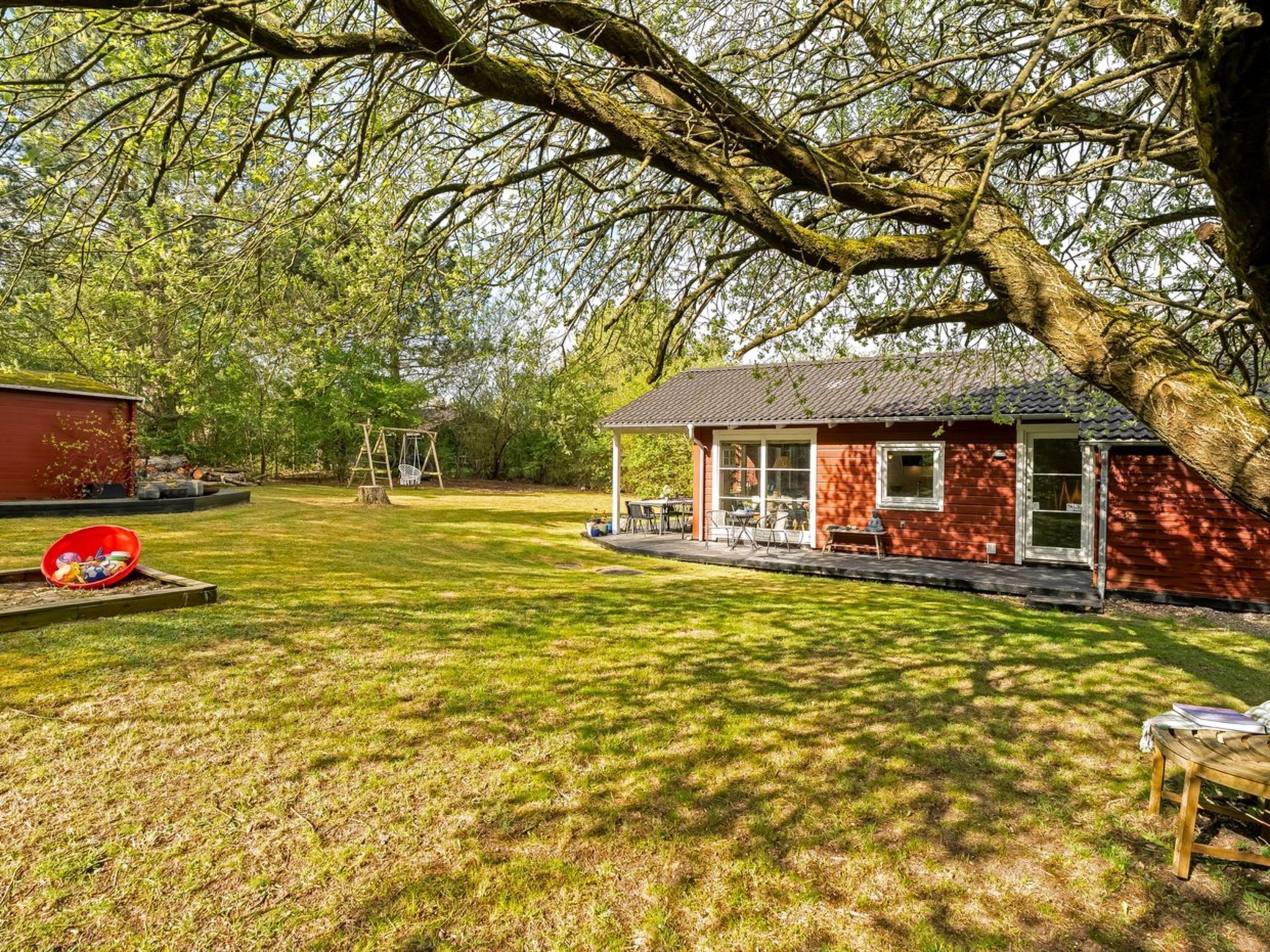A red wooden cabin with a porch, surrounded by a grassy yard and trees.