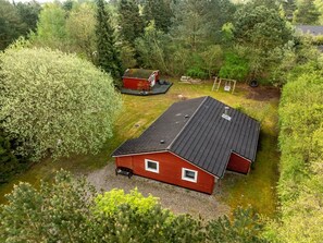 Een rood gebouw met een schuin dak, omgeven door weelderige begroeiing en bomen.