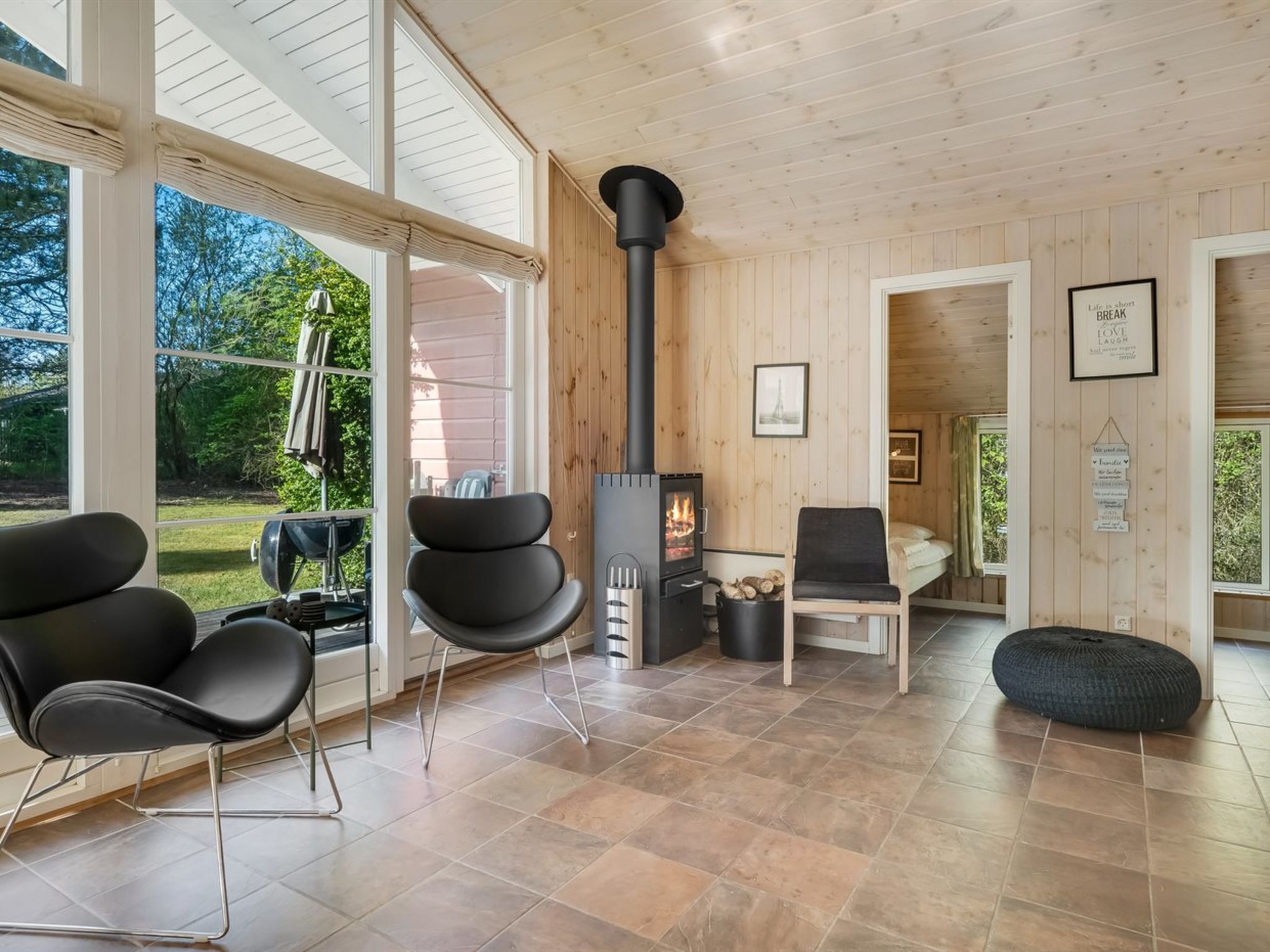 A modern interior with a wood-burning stove, large windows, and a cozy seating area.