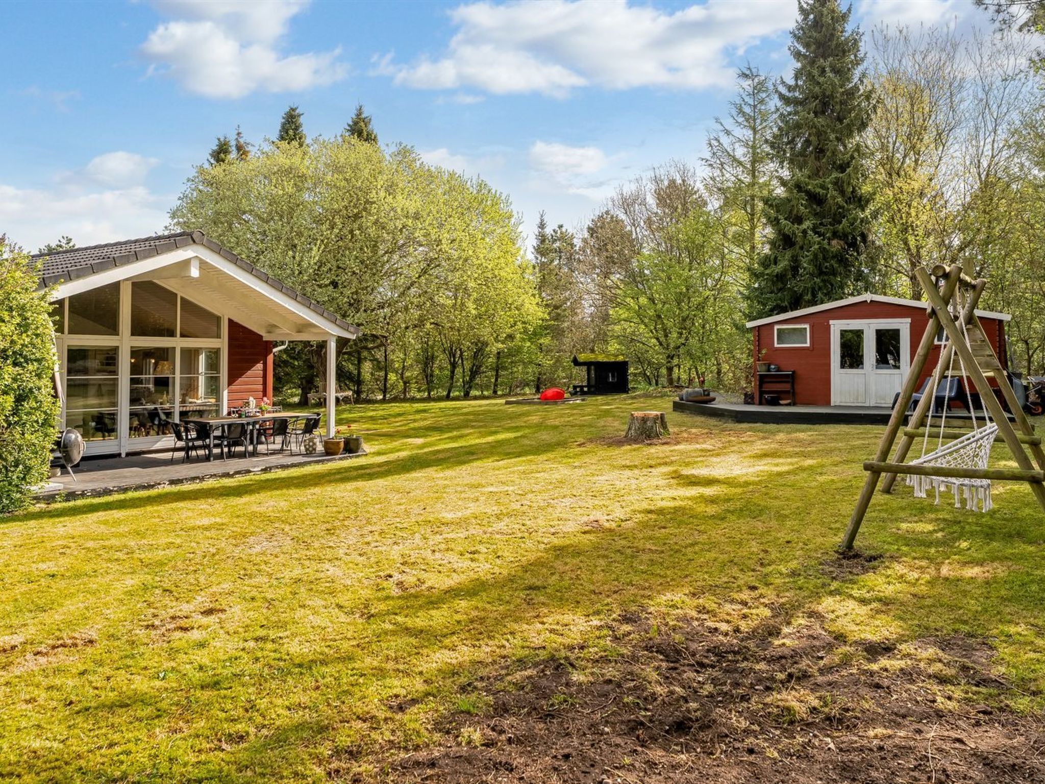 Un amplio espacio al aire libre con una mesa y sillas de comedor, un edificio pequeño y un conjunto de columpios.