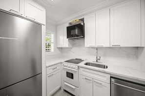 A compact kitchen with white cabinetry, a stainless steel refrigerator, a built-in oven, a microwave, and a dishwasher. - 1855 Managed by Brampton Park (Delray Beach)