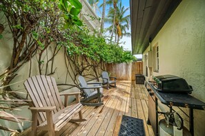 Een houten terras met stoelen en een barbecue, omgeven door groen en een houten hek.