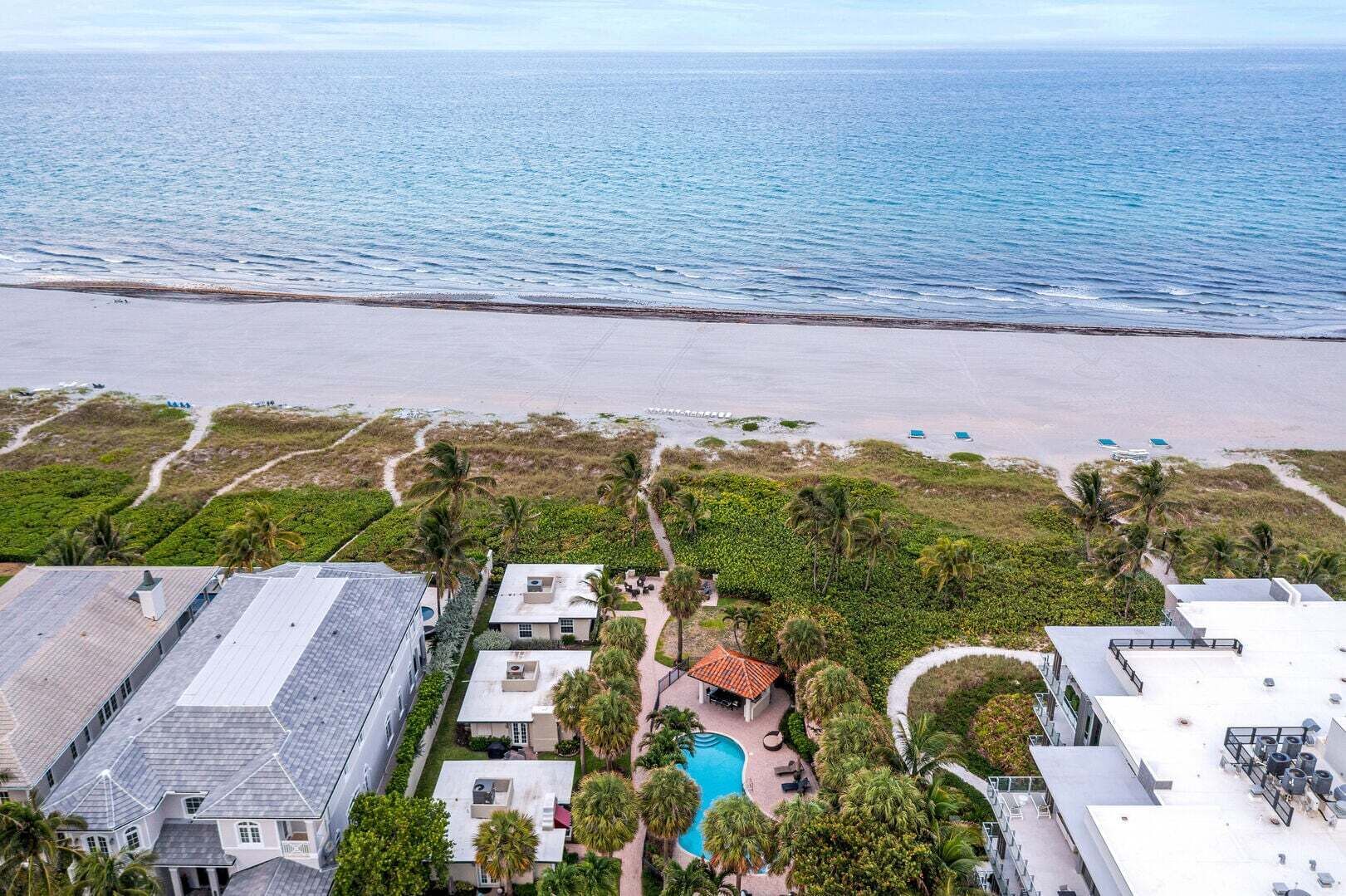An aerial view of a coastal property with a swimming pool, beach access, and a view of the ocean.