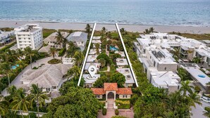 Vista aérea de una zona residencial costera con playa, palmeras y una combinación de arquitectura moderna y tradicional.