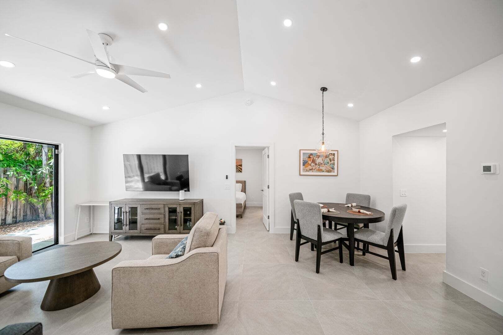 A modern living room with a dining area, a TV mounted on the wall, and a ceiling fan.