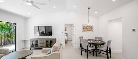 A modern living room with a dining area, a TV mounted on the wall, and a ceiling fan.