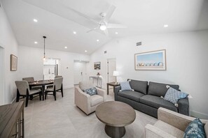 Ein modernes Wohnzimmer mit grauem Sofa, zwei Sesseln, einem Couchtisch und einem Essbereich mit Tisch und Stühlen.