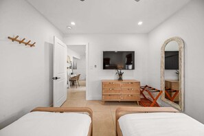Quarto com duas camas, cômoda, televisão e espelho.
