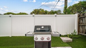 Ein Weber Spirit Grill mit digitalem Thermometer und Bedienelementen vor einem weißen Zaun und einem grünen Rasen.
