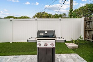 Ein Weber Spirit Grill mit digitalem Thermometer und Bedienelementen vor einem weißen Zaun und einem grünen Rasen.