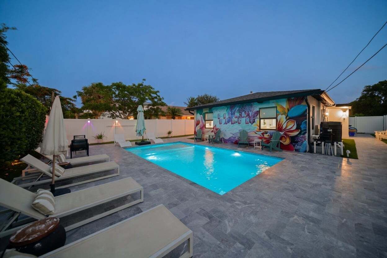 A swimming pool with lounge chairs, a mural, and a small building with a sign.