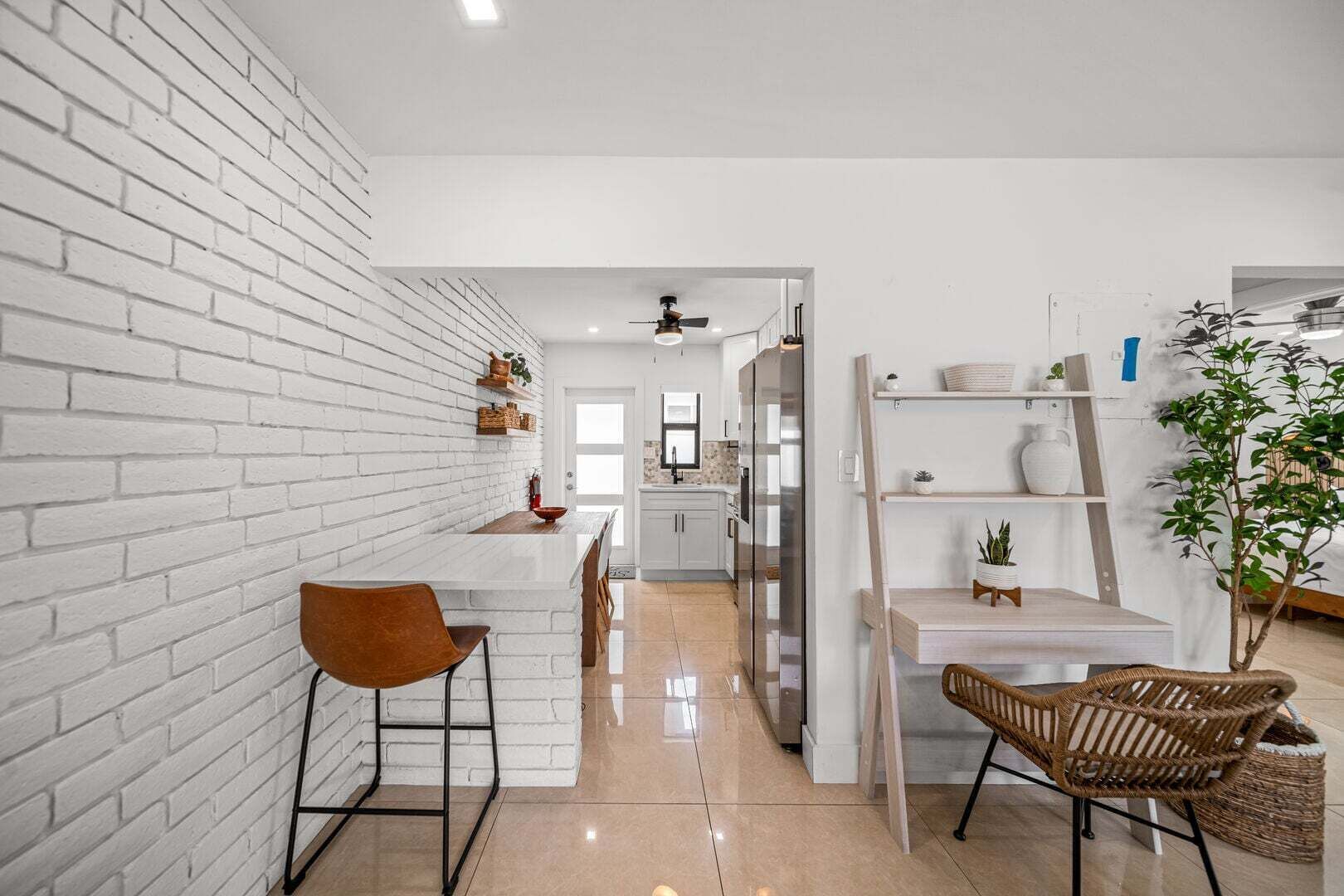 A modern kitchen with white brick walls, a central island, and a dining area with wicker chairs.