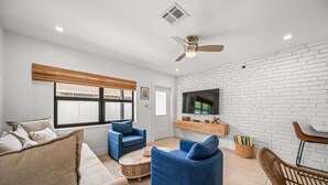 Un salón con sofá, dos sillones, una mesa de centro, televisor y pared de ladrillo.