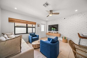 Uma sala de estar com sofá, duas poltronas, uma mesa de centro, televisão e uma parede de tijolos.