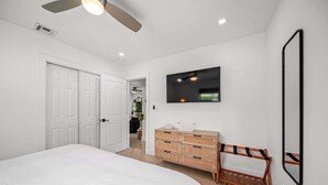 Un dormitorio con cama, cómoda, televisor y ventilador de techo.