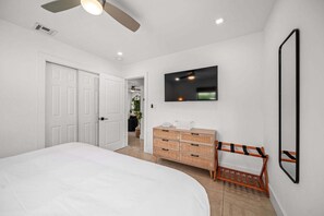 Ein Schlafzimmer mit Bett, Kommode, Fernseher und Deckenventilator.
