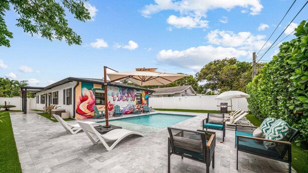 Un área de piscina moderna al aire libre con sillas de descanso, un mural y una zona de estar cubierta.