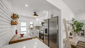 Cocina moderna con armarios blancos, refrigerador de acero inoxidable e isla de madera.
