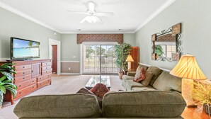 A living room with a sofa, a television, and a ceiling fan. - Golf Villa Near Beach at Myrtlewood | Magnolia Pointe Luster Leaf 4890-304 (Myrtle Beach)