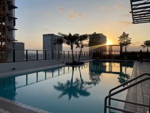 Une piscine sur le toit offrant une vue imprenable sur le coucher du soleil, entourée de bâtiments modernes et de palmiers.