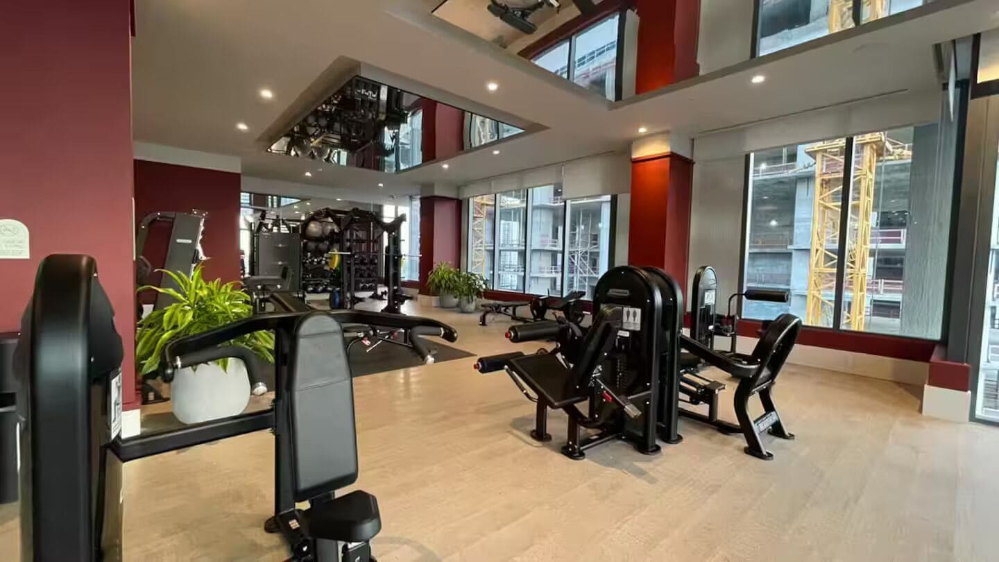 Ein Fitnessstudio mit Trainingsgeräten, großen Fenstern und hoher Decke.