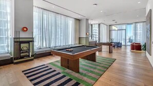 A modern living room with a pool table, a fireplace, and large windows. - Entire apartment in Miami – NEW (Miami)
