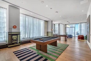 Ein modernes Wohnzimmer mit Billardtisch, Kamin und großen Fenstern.