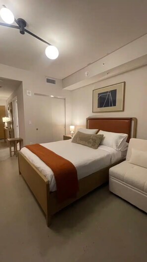 Une chambre d’hôtel avec un lit, une table de chevet, une lampe, une chaise et un luminaire au plafond.