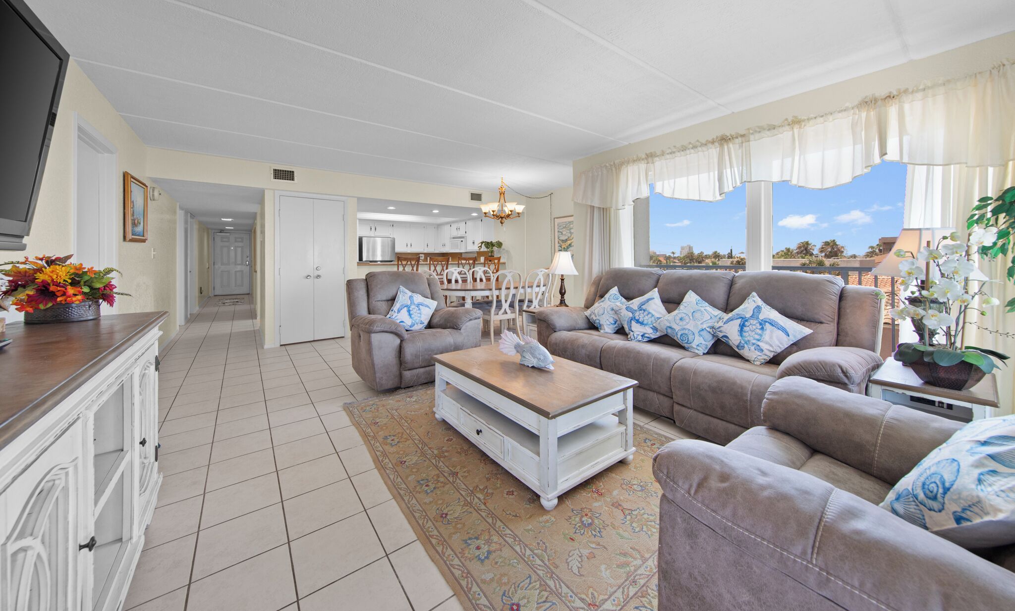 A living room with a sofa set, a coffee table, a TV, and a kitchen in the background.