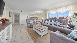 A living room with a sofa set, a coffee table, a TV, and a kitchen in the background. - Beachfront 3BR/3BA condo with Gulf views in South Padre Island. (South Padre Island)