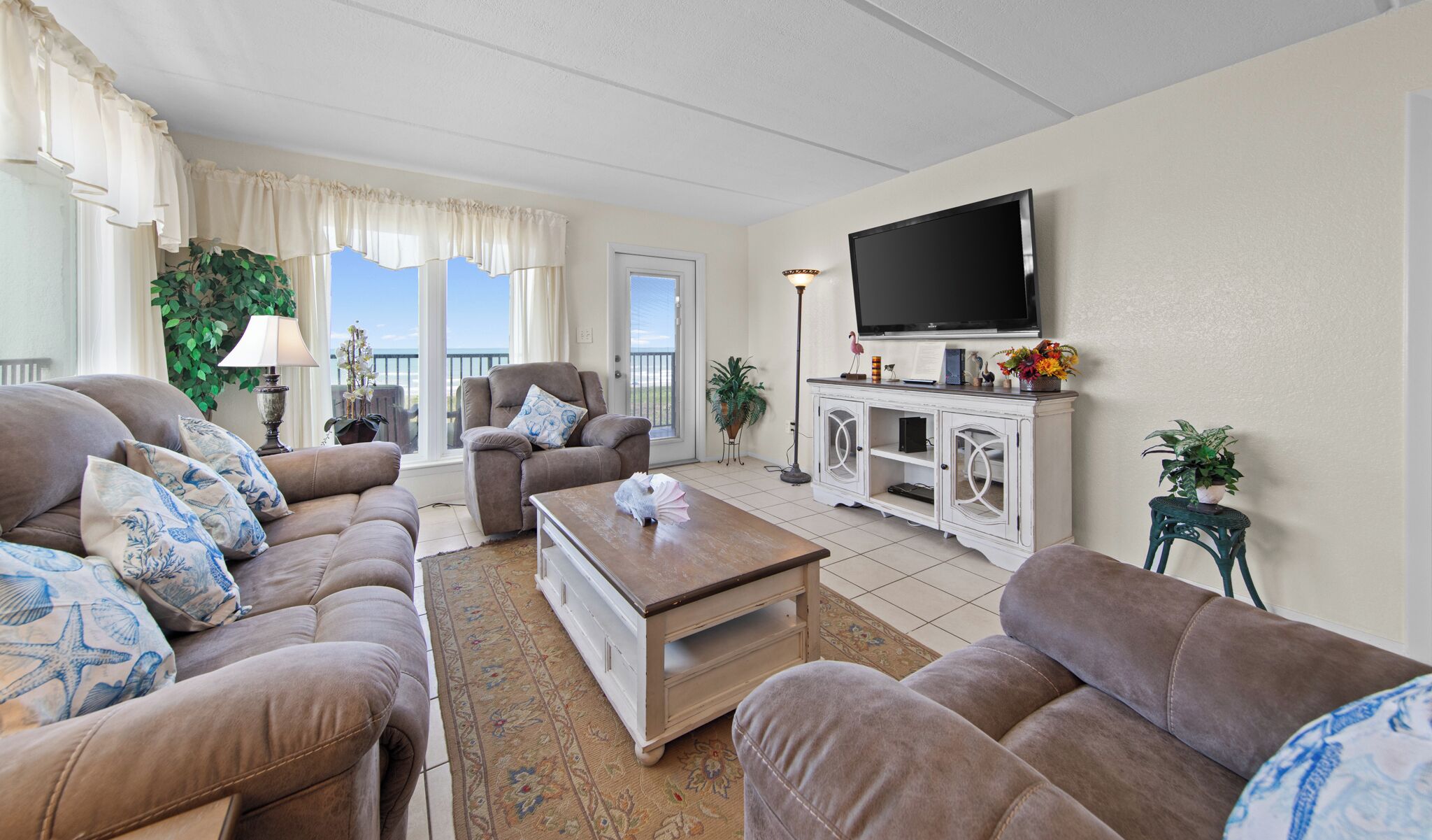 Ein Wohnzimmer mit einer Sofagarnitur, einem Couchtisch, einem Fernseher und einem Balkon mit Aussicht.